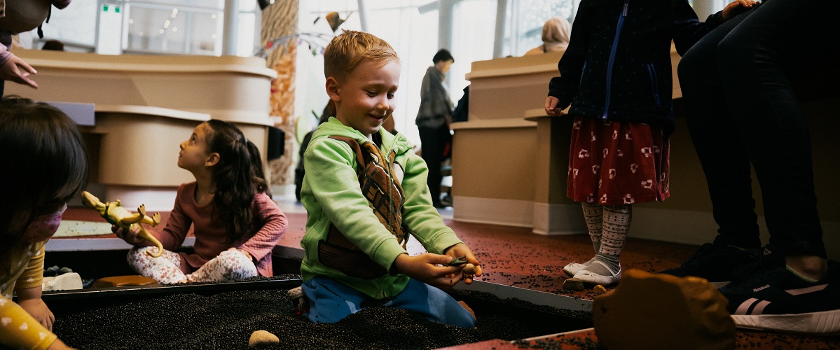 Children play in the Dig Pit - a recessed section of floor filled with small black beads, and plastic toys