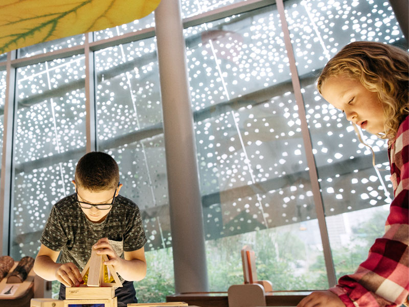 A boy and girl play intently with blocks on a light table. 