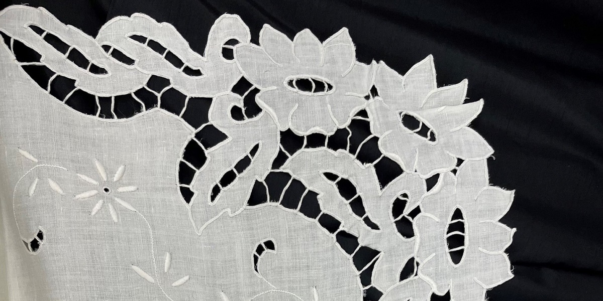 A close up of a white embroidered lacey fabric, resting on a black background.