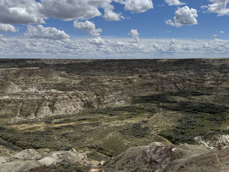 A vast expanse of dry hilly land and blue skies filled with puffy white clouds
