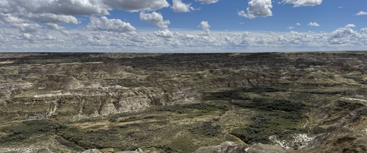 A vast expanse of dry hilly land and blue sky with puffy white clouds.