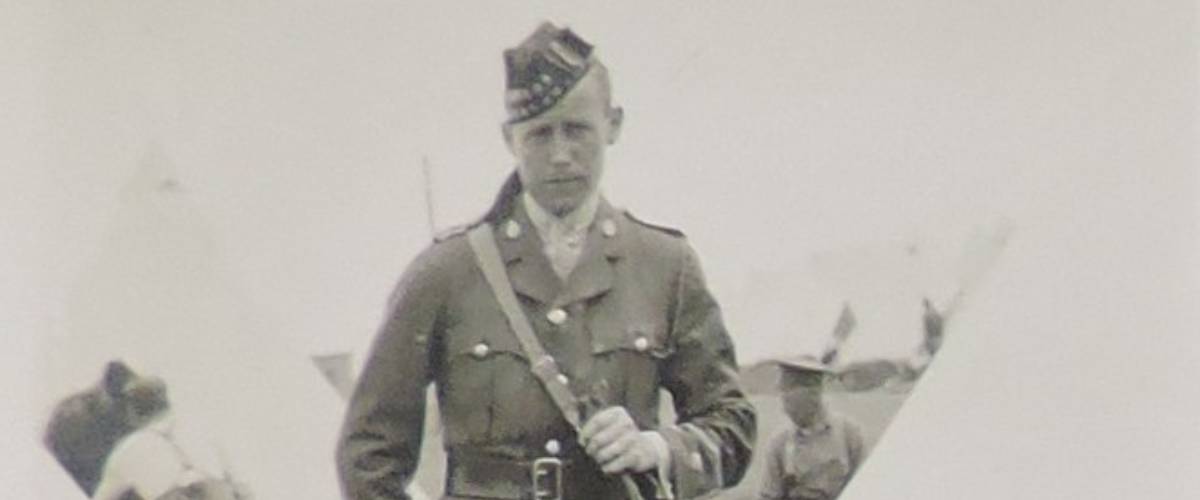 A faded vintage photograph of Solider William Frame looking stoically out at the camera. He is wearing his military uniform. You can see tents in the background.