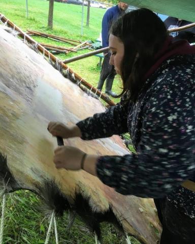 A hide is stretched across a frame, while Coral, RAM's Steward of Indigenous Collections, uses a tool to scrape the hide. 