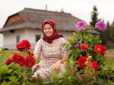 photo of a woman kneeling amongst flowers with a house in the background