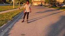 A young man on rollerblades skates casually toward the camera on a quiet street.