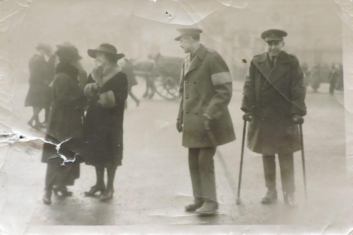 Two women on the left looking right, a man in military uniform looking right and a second man (William Frame) on the right looks directly at the camera. He is in his military uniform and is using crutches.