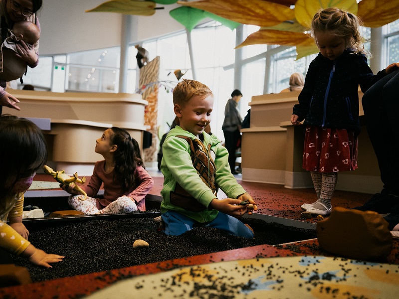 Children play in the Dig Pit - a recessed section of floor filled with small black beads, and plastic toys