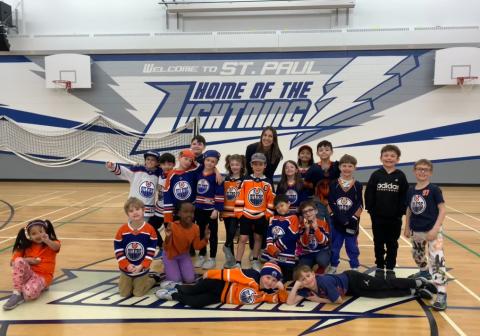 A group of students wearing Edmonton Oilers jerseys and sweaters stand facing the camera. The students are standing in a school gym.
